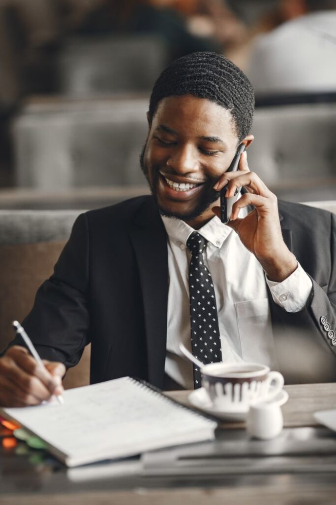 Mastering the First Impression: Your intriguing post title goes here Smiling businessman talking on phone while taking notes in a modern office setting.