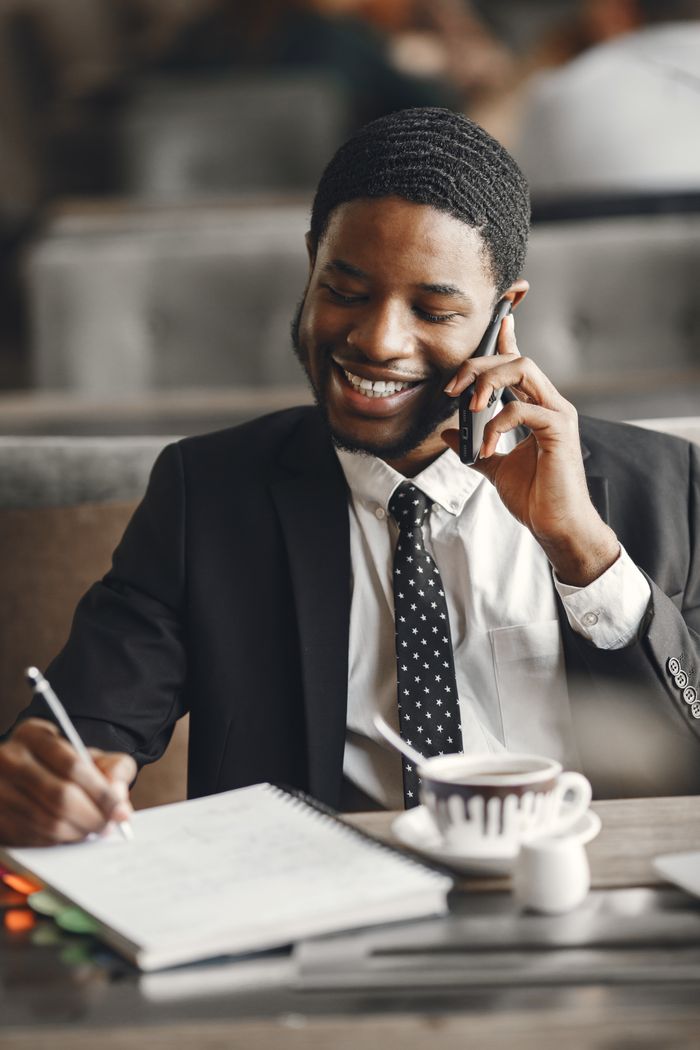 Mastering the First Impression: Your intriguing post title goes here Smiling businessman talking on phone while taking notes in a modern office setting.