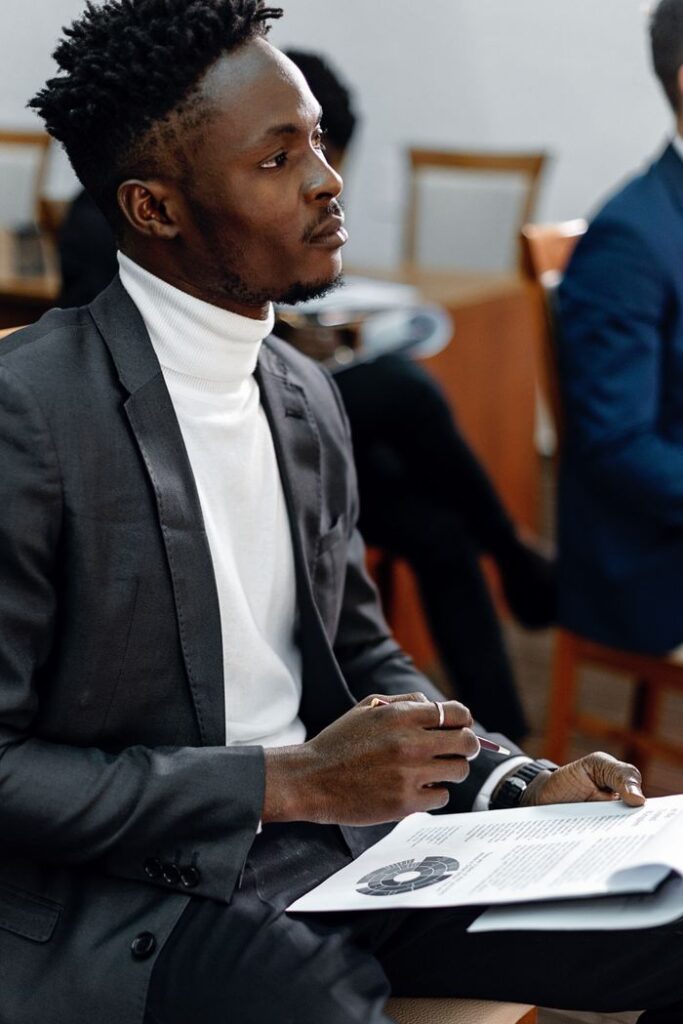 Crafting Captivating Headlines: Your awesome post title goes here Young professional in black suit attentively listening during a presentation, holding documents.